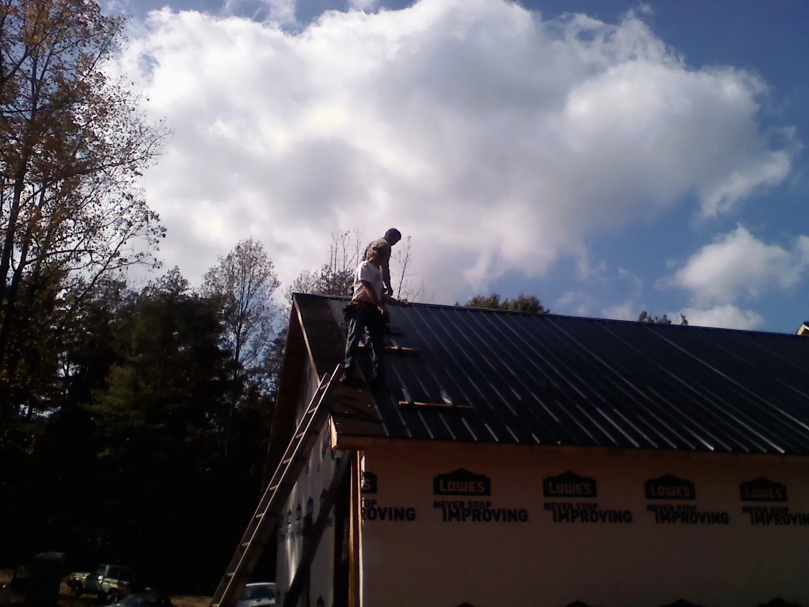 Roofer fastening dark metal panels high against a cloudy sky, from a Roof Inspection job in Forks Of Salmon